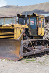 Yellow bulldozer rests on rocky ground with visible wear, surrounded by mountains and a clear sky, indicating a construction or mining site © Anat art