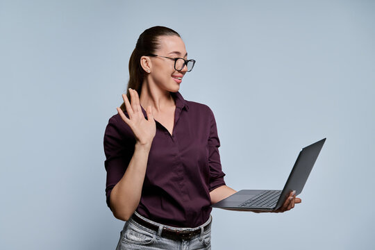 Young female student waving hand during video call on laptop studio portrait