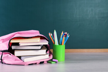 Backpack with books and stationery on white desk against chalkboard. Space for text © New Africa