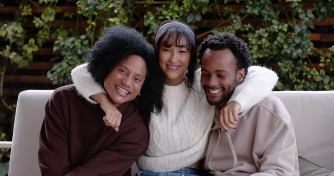 Diverse friends hugging with center wrapping arms, leaning in, smiling for group shot on patio sofa