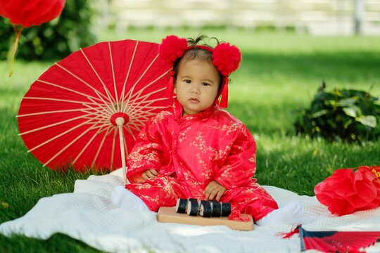 Asian baby in traditional red costume with umbrella, sushi rolls and lantern on picnic blanket