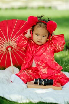 Asian baby in traditional red costume with umbrella, sushi rolls and lantern on picnic blanket
