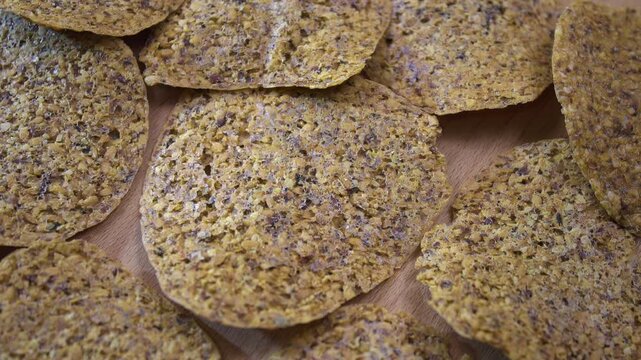 Pile of dehydrated fruit and seed crisps rotating on wooden surface, top view