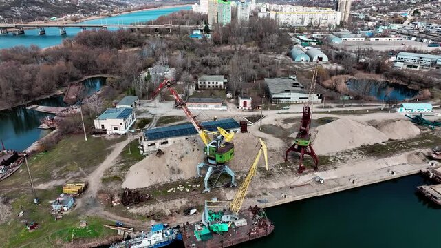 Rail-mounted portal cranes at a river-port quay in a drone aerial view. Inland waterway logistics and construction aggregate supply