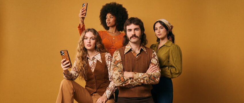 A group of stylish individuals, inspired by the 1970s era, pose for a photograph, showcasing retro fashion and a playful mood with one person holding up a smartphone.