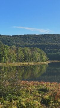 Scenic water drone view at Sherman Reservoir Boat Launch, Vermont, USA, with forested mountains, tree reflections and clear sky. Peaceful nature and boating recreation. 4K. Vertical.