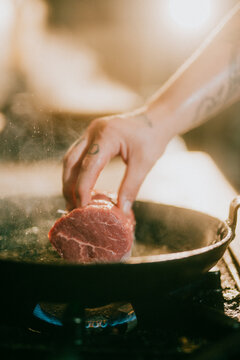 Chef's hand flips a steak in a hot cast iron skillet