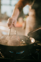 Fototapeta premium Chef uses tongs to flip meat in a pan on a gas burner
