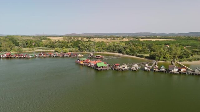 Lake Bokod floating village in Bokod, Hungary, with fishing huts, stilt houses and wooden piers on the cooling reservoir, surrounded by forest and fields, filmed by drone.