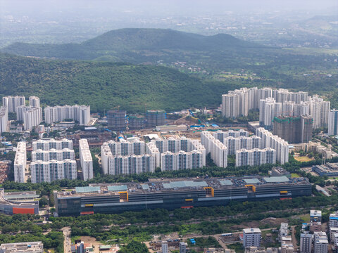 Aerial view of Hinjewadi Phase III featuring modern high-rise residential apartment complexes and large office buildings surrounded by lush green hills in Pune, Maharashtra, India.