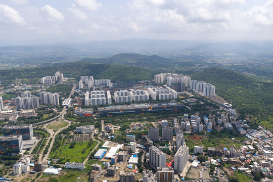 Aerial view of Hinjewadi Phase III featuring modern residential complexes, office buildings, and lush green hills under a cloudy sky in Pune, Maharashtra, India.