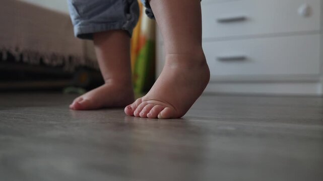 Close up of a toddler taking first steps on a wooden floor in a bright home interior setting