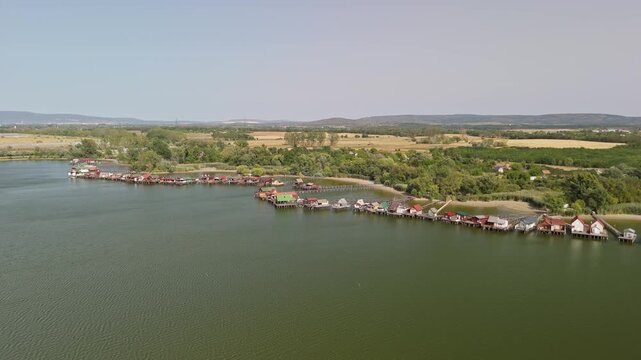 Lake Bokod in Hungary with floating village fishing cabins and stilt houses on the cooling reservoir, wooden piers and green shoreline landscape in aerial view.