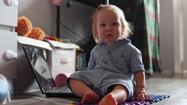 A curious toddler sitting on the floor and looking at a laptop screen in a bright home interior