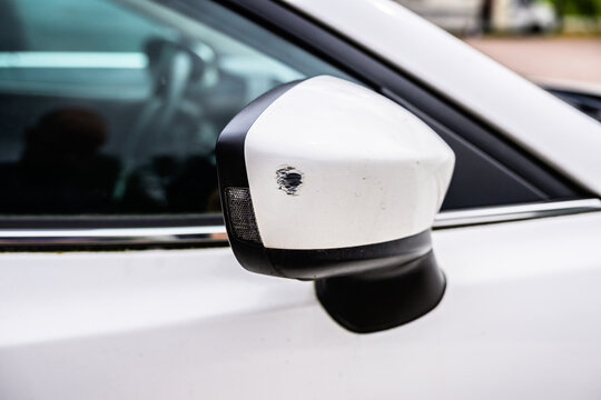 Scratched white car side mirror showing minor collision damage.