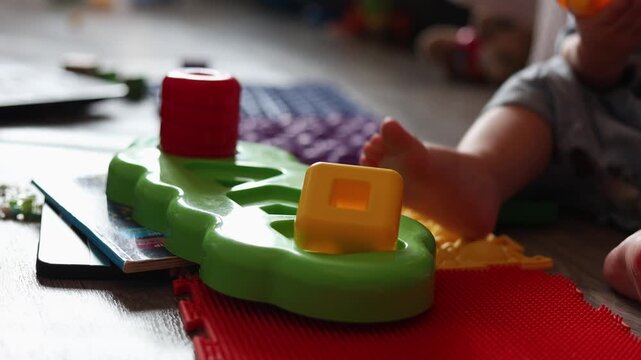 A toddler plays with a colorful plastic shape sorting toy on a textured floor in a bright room