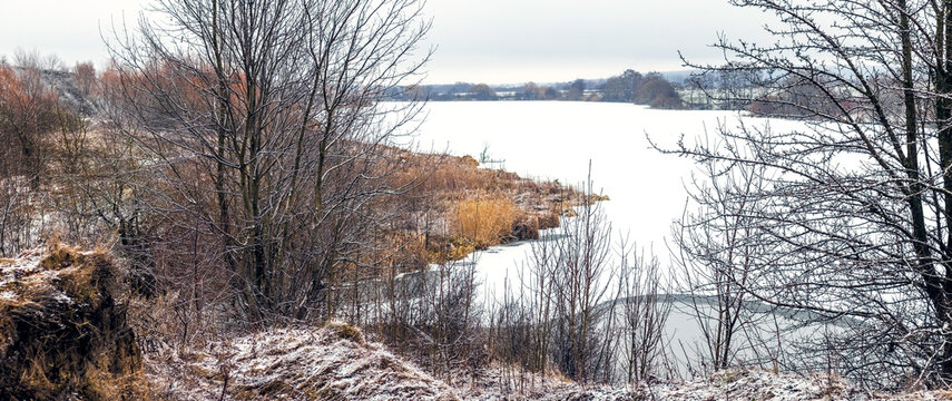 Winter landscape with lake, snow covered shore and trees in foreground