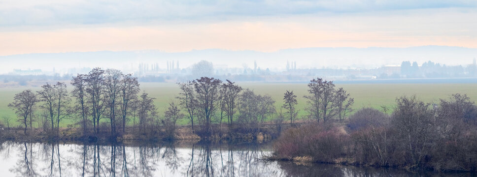 Autumn landscape with trees, water reflection and hazy horizon in background
