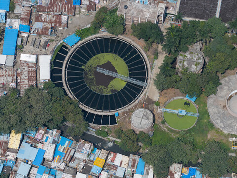 Aerial view of the PCMC Waste Water Treatment Plant with circular sedimentation tanks, surrounded by dense urban housing with metal rooftops and trees in Pimpri-Chinchwad, Maharashtra, India.