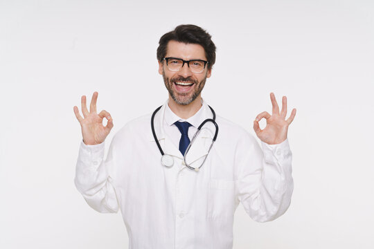 Portrait of doctor, general practitioner, physician, medical professional wearing white uniform coat and stethoscope, posing with okay gesture and smiling isolated on white studio background