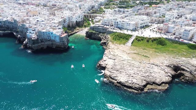 Polignano a Mare, Puglia, Italy. Lateral aerial drone flight along the cliffside old town, rocky coast and turquoise Adriatic Sea with motorboats.