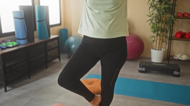 Woman pressing hands together and balancing in tree pose on a yoga mat in a studio; serenity balance.