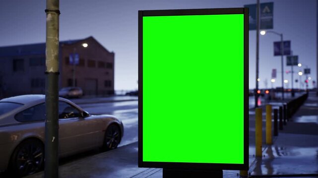 Blank green screen city light billboard on a city sidewalk in the blue hour before sunrise, clear sky. Timelapse of passing traffic with shallow depth of field and soft bokeh. Chroma key mockup for