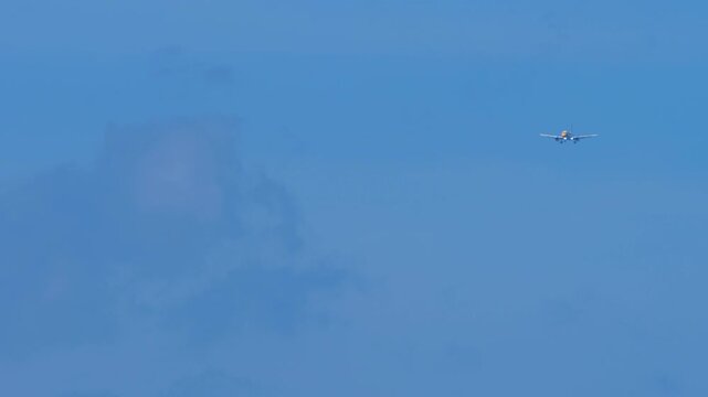 Commercial passenger airplane flying in clear blue sky during daytime approach, telephoto view of twin-engine jetliner in flight