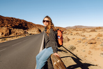 Female traveler with backpack leans against roadside barrier in remote, open landscape. Woman is resting at sunset in national park near volcano. Adventure and wilderness themes. © maxbelchenko