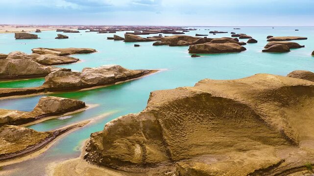 Yardang landforms rise out of turquoise water under bright daylight, with textured sandstone mounds stretching toward the distant horizon.