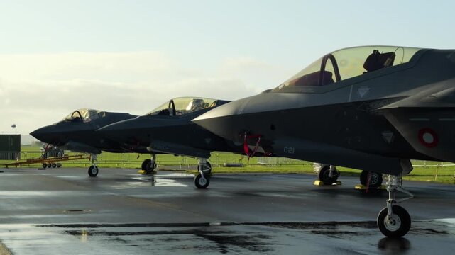 Three F-35 fighter jets parked on a wet runway