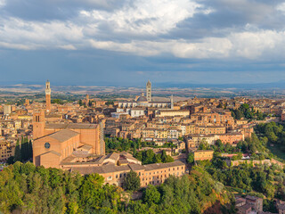 Fototapeta premium Aerial view of the Italian famouse city Siena with the landmarks of Basilica di San Domenico, Piazza del Campo tower and Duomo di Siena standing out over the old town center