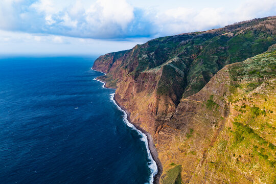 Atlantic coast of Madeira with extensive cliff walls, Portugal. Aerial footage of island coastline beneath coastal plateau