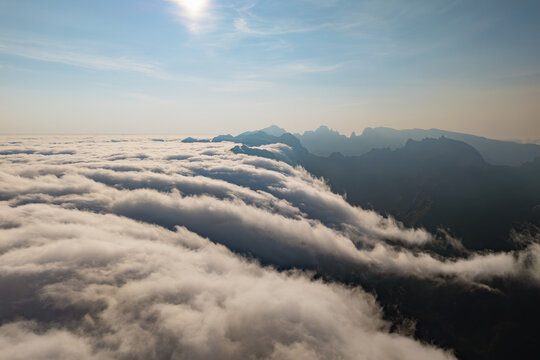 Dense clouds advancing over mountain ridges and spilling down into valleys. Aerial view above encroaching cloud cover