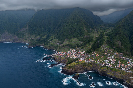 Seixal coastal settlement in Madeira, Portugal, elevated aerial view. Village extends along rocky shoreline below terraced mountain slopes