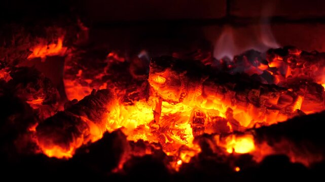 Close-up ember glow and flickering cinders over hot charcoal bed, crackling texture and warm dramatic lighting for fireplace and heat atmosphere