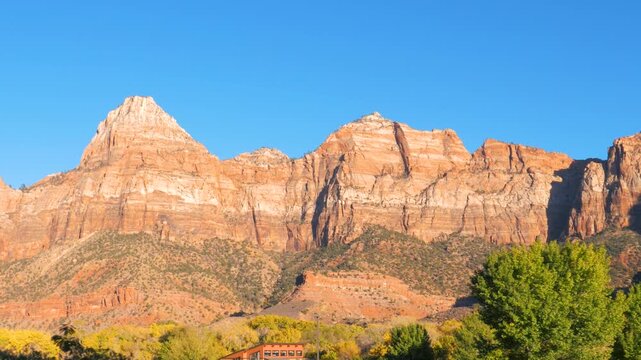 Beautiful view of red rock cliffs of zion national park in utah while driving, with iconic peak of watchman mountain against a clear blue sky during a sunny autumn day