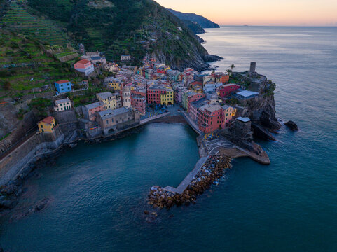 Aerial view of the colorful village of Vernazza nestled in the cliffs of the Cinque Terre coastline with a stone pier extending into the Ligurian Sea, Vernazza, Liguria, Italy.