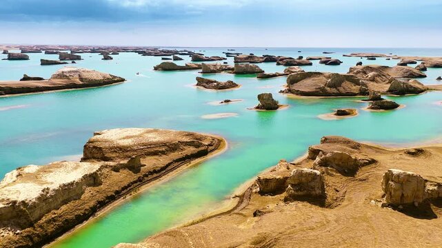 Eroded yardang landforms rise above vivid turquoise water under a blue sky, illuminated by bright daylight across the arid desert lake.