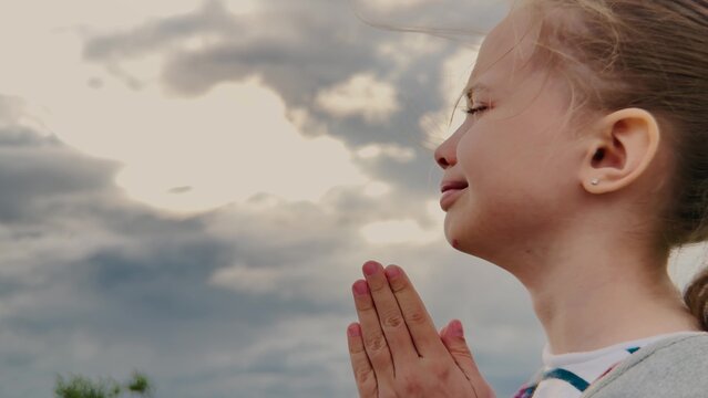 Heart of a Child in Prayer, Girl s Gentle Faith, Praying Under a Cloudy Sky, Silent Plea for Help, Graceful Hope in Youth, Innocent Spirit on Display, Pure Emotion Outdoors, Sweet and Serene Prayer