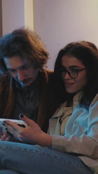 Couple sharing smartphone indoors, browsing together and enjoying mobile entertainment, quality time and connected digital lifestyle. Vertical video. 