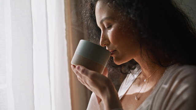 Expecting mom drinking coffee window. Close up hand caressing pregnant belly.