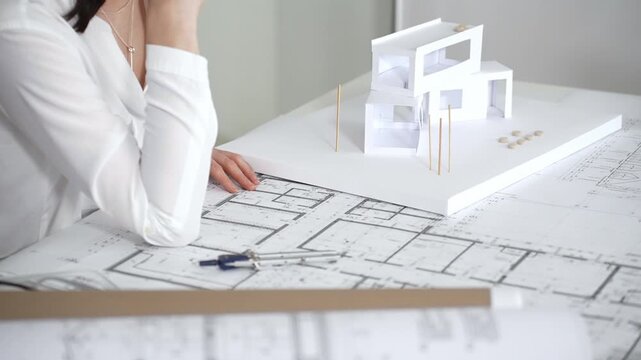 Architect's hands working on desk, comparing paper blueprints with digital floor plans on a laptop, using tools for precise measurements in architectural design
