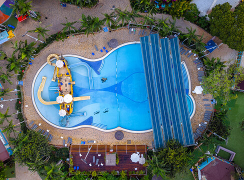 Aerial view of the Shefayim Water Park featuring a large swimming pool with a pirate ship play structure, water slides, sun loungers, and palm trees in Shefayim, Center District, Israel.