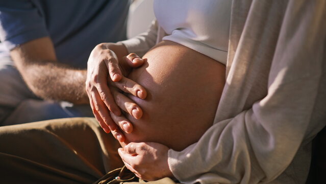Close up expectant parents cradling pregnant belly. Hands on baby bump sunlight.