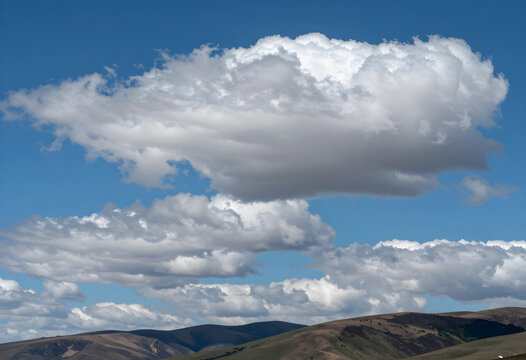 Climate change and weather patterns, white cumulus clouds over dry rolling hills in a vast landscape with clear blue sky and environmental atmosphere