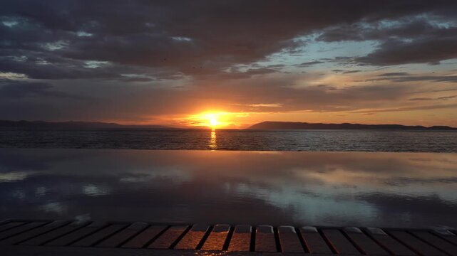 Golden sunset over Adriatic Sea with flying birds and vivid reflection across calm modern infinity pool water