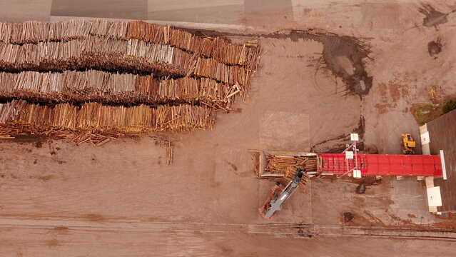 Aerial view of a paper mill with large stacks of logs and industrial machinery operating near a red conveyor system in Graz, Styria, Austria.