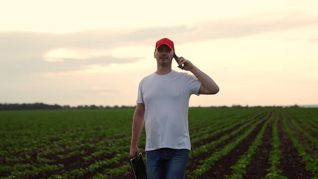 Agriculture, Agricultural Worker in Sunset Light, Farm worker connecting by phone, sunset creates warm ambiance, crop rows visible, focused expression, holding device confidently, modern farm