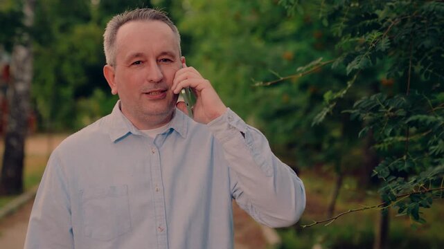 joyful caller outdoors, cheerful phone user outside, smartphone in hand, forest backdrop setting., happy man chatting by phone, standing outside amid lush natural surroundings., casual man on mobile